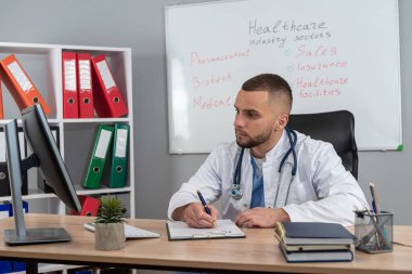 Genç doktor ya da pratisyen hekim klinikteki hasta dosyalarında çalışıyor. Hastalık tedavisi