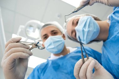 Diş çekmek için dişlerini tutan dişçi ve asistanı hastaya bakıyor. Ameliyat yapan tıbbi ekip.