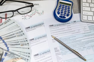 1040 dolar vergi formları, kalem hesap makinesi ve para bardakları masada. Vergilendirme, vergi ödeme. Nisan zamanı.