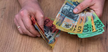 Avustralya Doları 'ndaki banknotları tahta masa arkasında tutan bir iş adamı. Finansal tasarruf kavramı