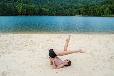Spor giyimli beyaz kadın göl kumsalında egzersiz yapıyor. Yaz zamanı. Kilo verme egzersizi