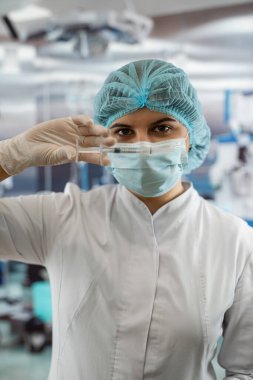 Hemşire portresi beyaz önlük, şapka ve eldiven giyer ve bir hastayı tedavi etmek için bir hastane odasında ilaç enjekte etmeye hazırlanır.