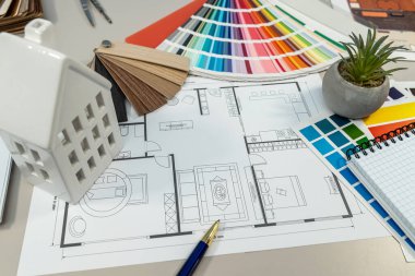 Masanın üzerinde, temel proje aracı olarak görev yapan bir evin yerleşim ve tasarım özelliklerini gösteren ayrıntılı bir kat planı var.