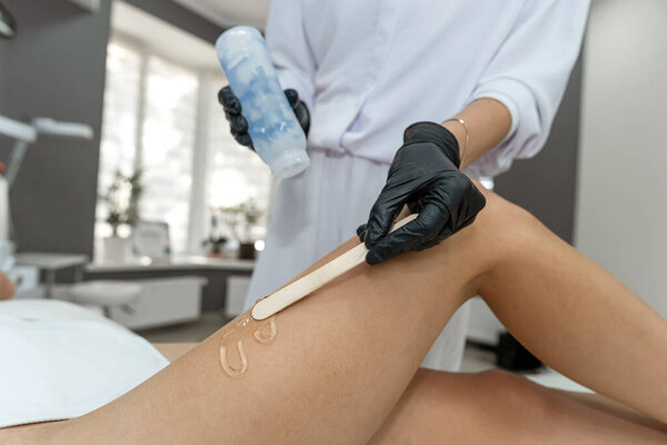 At a wellknown salon, a highly skilled woman meticulously waxes another clients legs to achieve smooth, flawless, and visually pleasing skin