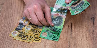 Avustralya Doları 'ndaki banknotları tahta masa arkasında tutan bir iş adamı. Finansal tasarruf kavramı