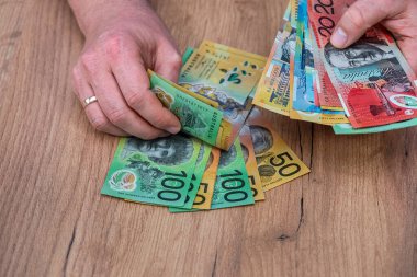 Avustralya Doları 'ndaki banknotları tahta masa arkasında tutan bir iş adamı. Finansal tasarruf kavramı