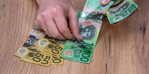 Avustralya Doları 'ndaki banknotları tahta masa arkasında tutan bir iş adamı. Finansal tasarruf kavramı