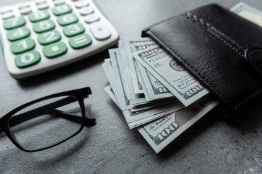 Üzerinde dolar banknotları ve hesap makinesi gözlükleri olan siyah cüzdan. Paranın mali hesaplamaları