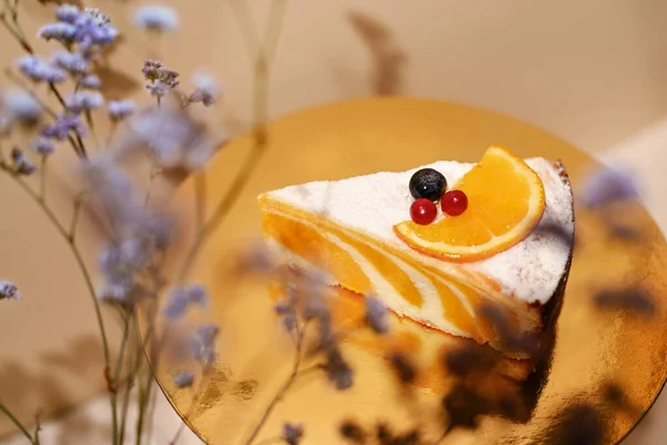 Composition with a piece of cake and flowers. A piece of pumpkin pie on a golden round shaped surface, blue dried flowers around it.