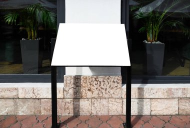 Binanın önündeki boş beyaz reklam standı. Dükkan pencereleri ve bitkilerle dolu. Kafe menüsü, mağaza promosyonları, reklamlar ya da hoş geldin mesajları için düzenleme. Tasarımınız için boşluk.