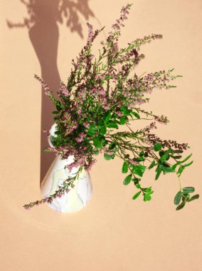 Şeftali kaplama vazoda pembe calluna buketi. Calluna vulgaris çiçekleri tamamen çiçek açmış. Heather 'ın dalları. Minimalist çiçek konsepti. Şeftali estetiği. Pembe ling, basitçe heather. Kart, düzen.