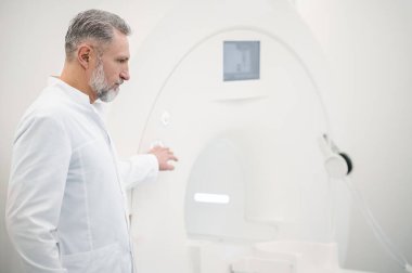- MRI. MRI tarayıcısının yanındaki laboratuvar önlüklü beyaz saçlı erkek doktor.