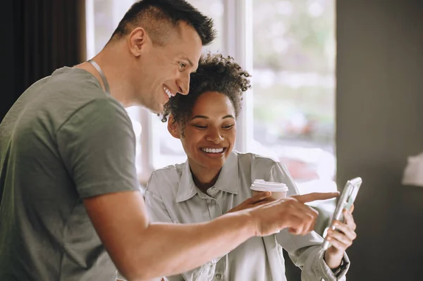 stock image Smiling employee demonstrating something on the smartphone to his pleased colleague with the paper cup