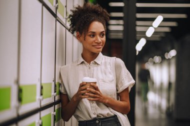 Dolaba yaslanmış kağıt bardakla gülümseyen, rüya gibi güzel bir kadının belden yukarı portresi.