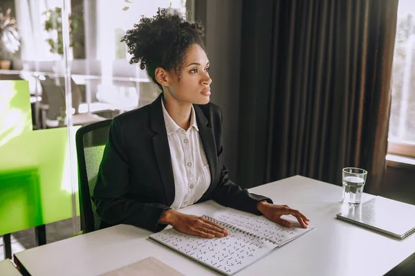 stock image Calm focused female employee touching with both hands raised dots in the open wire-bound notebook