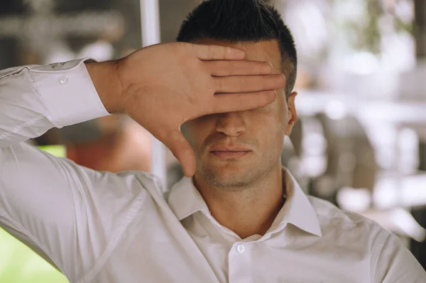 Portrait of a serious Caucasian man covering his eyes with the back of his hand