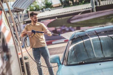 Müşteri otomobilinin dış yüzeyini yıkama makinesiyle temizleyen konsantre profesyonel bir otomobil işçisi.