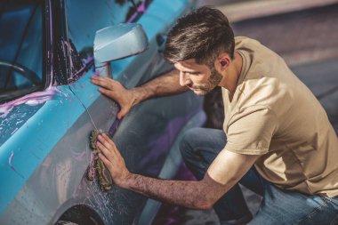 Profesyonel araba servisi çalışanı, bir motorlu aracın dış kısmını mikrofiber süngerle siliyor.