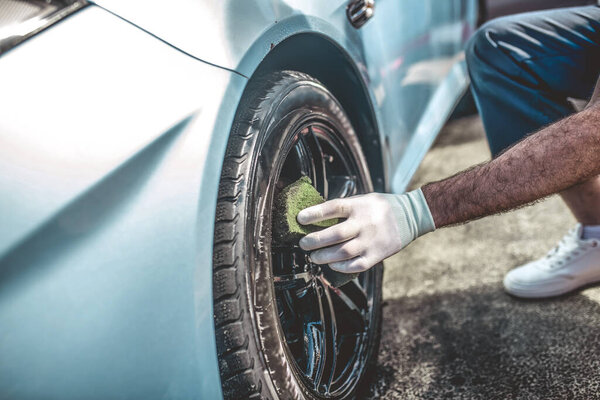 Cropped photo of a car detailer in the work glove wiping the car rim with a soft sponge