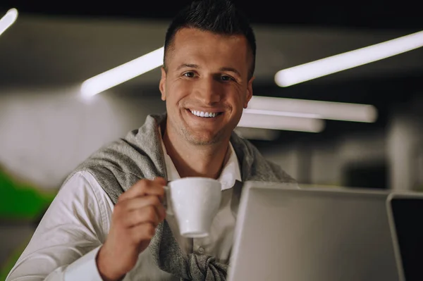 Αισιόδοξος Νεαρός Ενήλικος Ελκυστικός Άνδρας Πίνοντας Καφέ Δίπλα Στο Laptop — Φωτογραφία Αρχείου