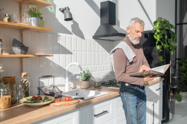 Resepsiyon aranıyor. Sakallı, olgun bir adam yemek kitabında resepsiyon arıyor.