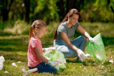 Çevre dostu. Genç kadın ve çocuğu parkta gargabe topluyor.