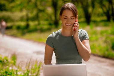 Uzaktan çalışıyor. Kadın salonda oturuyor, dizüstü bilgisayarla çalışıyor ve telefonla konuşuyor.