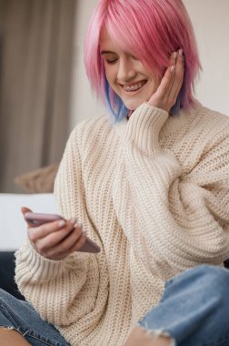 Joyous young woman seated on the floor in a room looking at the cellphone in her hands