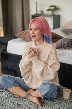 Joyful young pretty woman sitting cross-legged on the mat with the cellphone in her hands