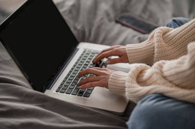 Cropped photo of a freelancer sitting on the bed while working on the portable computer