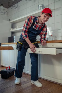 Smiling cheerful serviceman with a screwdriver in the hand leaning over the open cabinet drawer