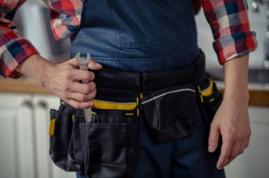 Cropped photo of a Caucasian serviceman taking a spanner out of the tool belt pocket