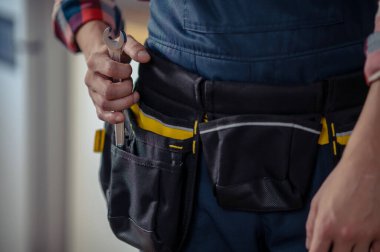 Cropped photo of a repair technician pulling a wrench out of the tool belt pocket