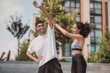 Smiling happy young man performing a side bend assisted by a professional female coach during the outdoor workout
