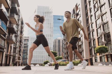 Low angle of a cheerful sporty young couple doing power walking in the city center