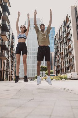 Low angle of a smiling athletic young man and his pleased fitness partner jumping upward
