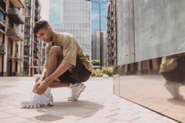 Serious focused jogger sitting on his haunches and tying the untied shoestring on his footwear