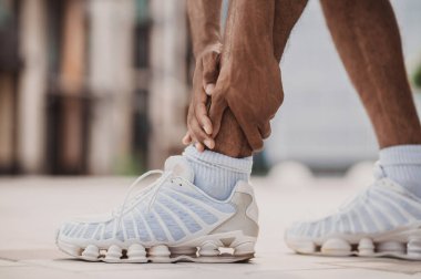 Cropped photo of an African American athlete touching his painful ankle after the morning run