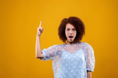 Look up. Cute young woman in a white blouse pointing her finger up