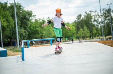 Serious concentrated preadolescent boy in protective gear trying to keep balance while riding on the skateboard