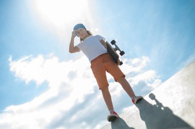 Low angle of a serious preadolescent boy with the skateboard in his hand posing for the camera against the sky