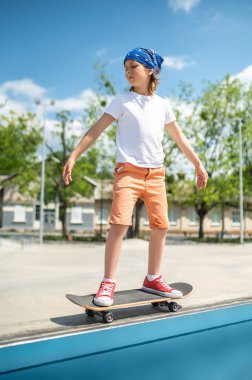 Full-size portrait of a serious focused preadolescent boy riding on the skateboard on the curb