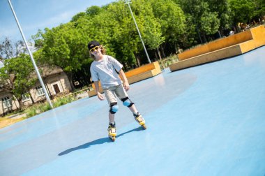 Full-length portrait of a preadolescent boy in sunglasses gliding across the rink on the roller skates