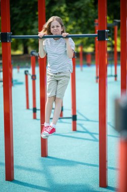 Full-size portrait of a cute strong preadolescent boy pulling up on the horizontal bar outdoors