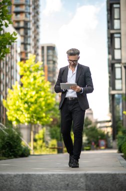 İşe koyulalım. Siyah takım elbiseli bir adam elinde tabletle yürüyor.