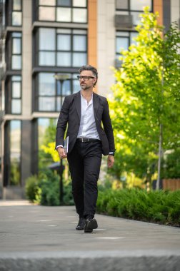 İşe koyulalım. Siyah takım elbiseli bir adam elinde tabletle yürüyor.