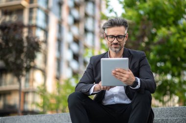 İnternette. Dışarıda elinde tabletle takım elbiseli şık bir işadamı oturuyor.
