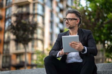 İnternette. Dışarıda elinde tabletle takım elbiseli şık bir işadamı oturuyor.