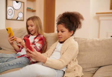 On internet. Kids sitting on the sofa with gadgets in hands and looking involved