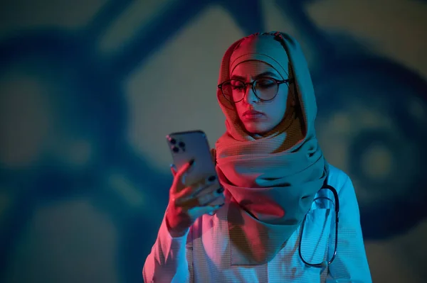 stock image Online doctor. Serious young female doctor in hijab with a phone in hand